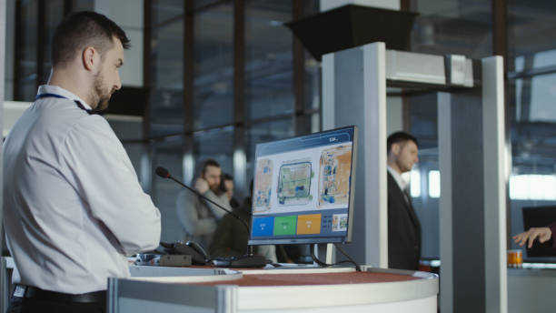 access control solution Man in uniform standing at counter at checking point and watching at monitor with x-ray of luggage.